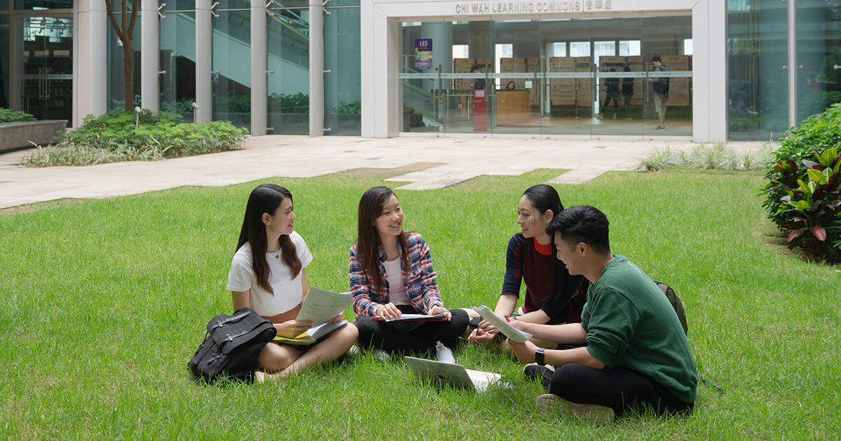 Students sitting in a group on the grass with school materials